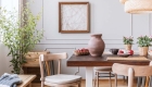 Clay vase on the table in a dining room interior with a plant, chairs and art on a wall